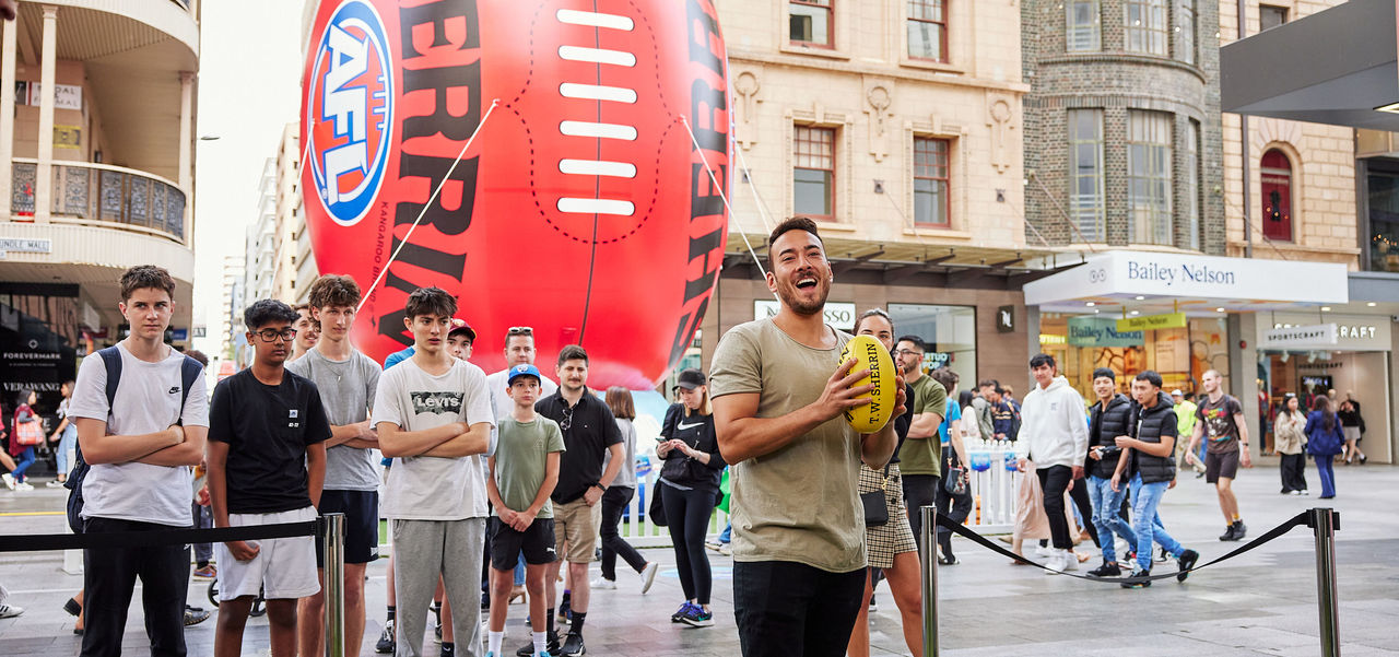 Person holding a footy in front of the giant AFL Sherrin Football