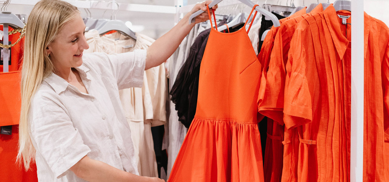 Woman holding a bright red coloured dress off a shopping rack