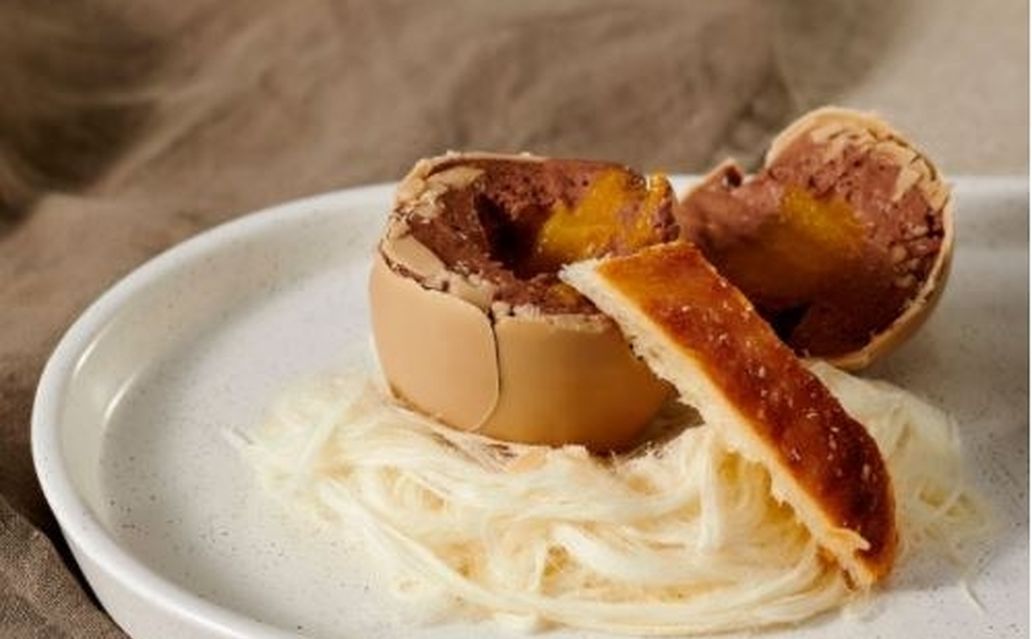 A chocolate egg opened to reveal mousse filling with pastry soldiers on a bed of fairy floss on a white plate