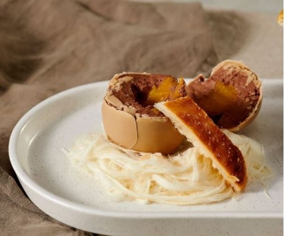 A chocolate egg opened to reveal mousse filling with pastry soldiers on a bed of fairy floss on a white plate
