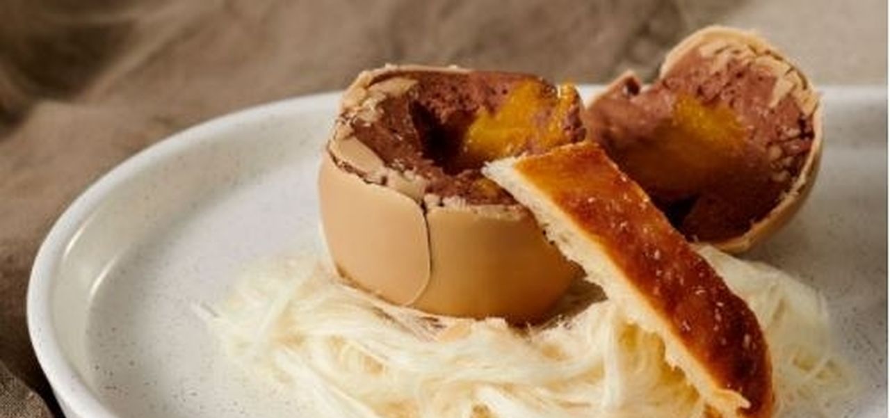 A chocolate egg opened to reveal mousse filling with pastry soldiers on a bed of fairy floss on a white plate