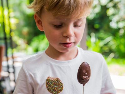 A young boy in a white t-shirt holding two chocolate pops