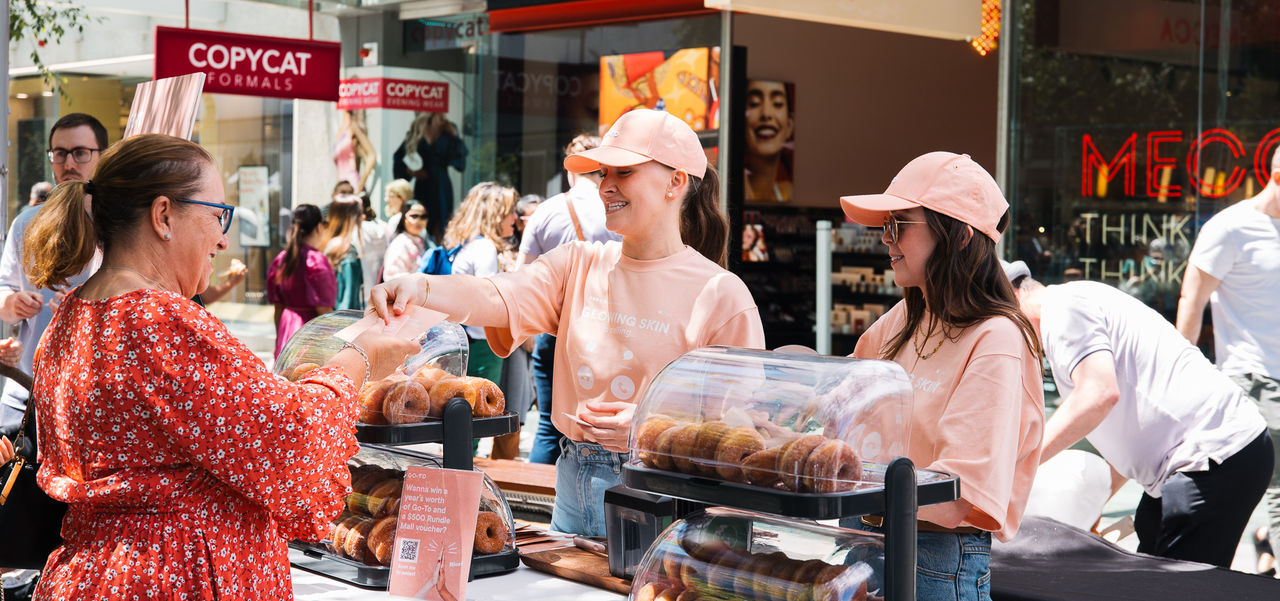 Two girls in Go-To skincare peach t-shirts handing out free cinnamon donuts