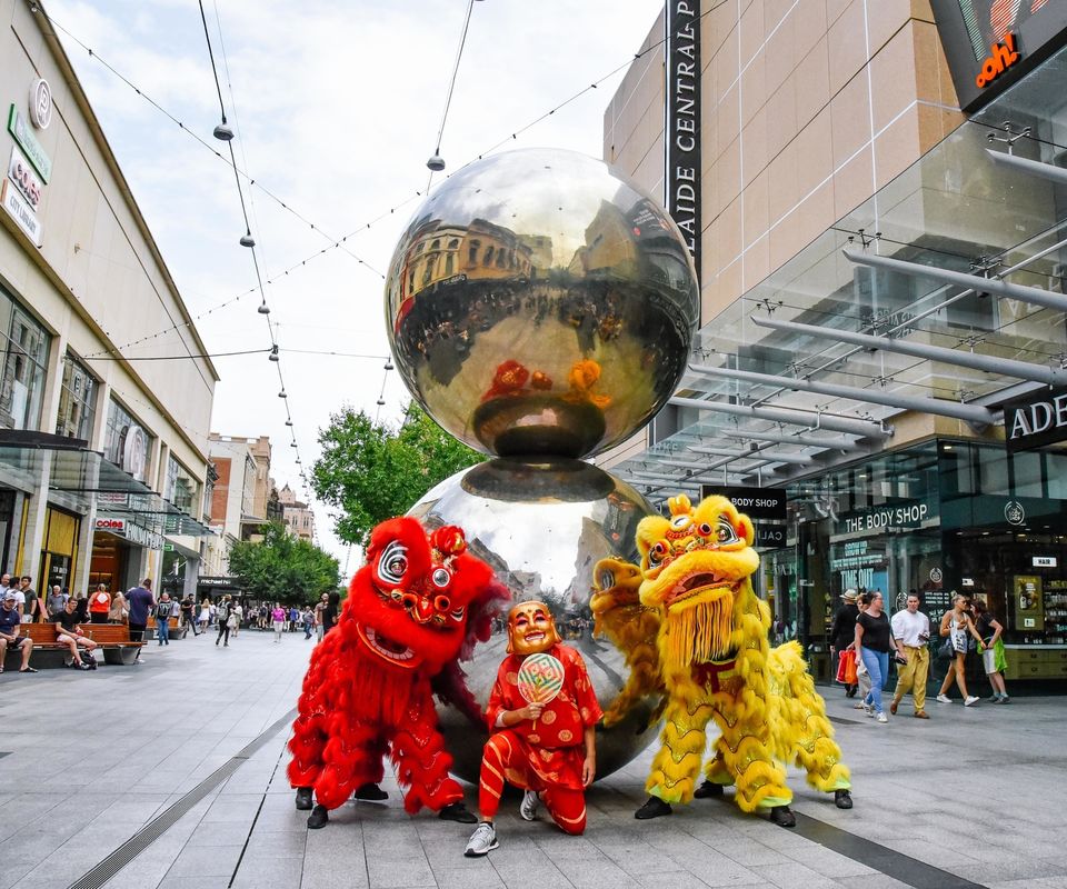 Two traditional lion dancers with the god of fortune in front of the Mall's Balls sculpture