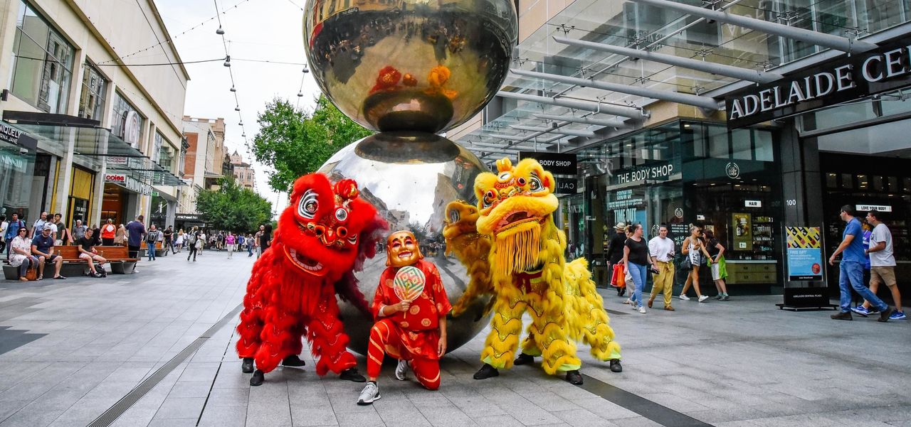 Two traditional lion dancers with the god of fortune in front of the Mall's Balls sculpture