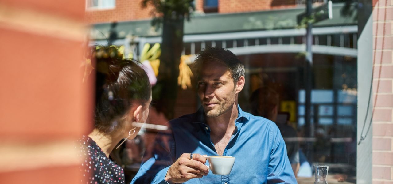 A man drinking coffee in a cafe with a woman