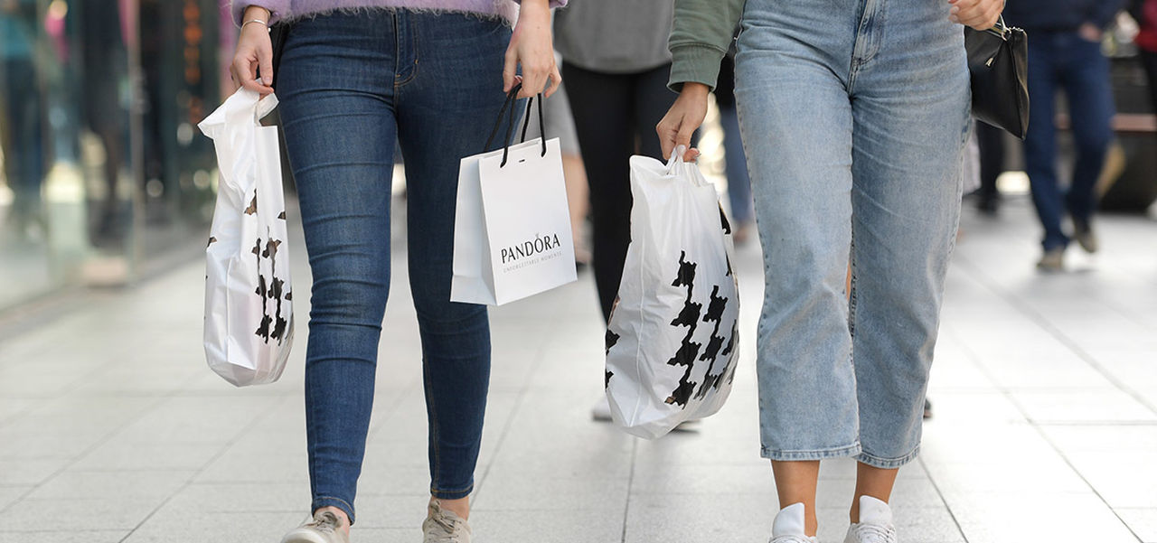 Two women's lower bodies with the women holding shopping bags