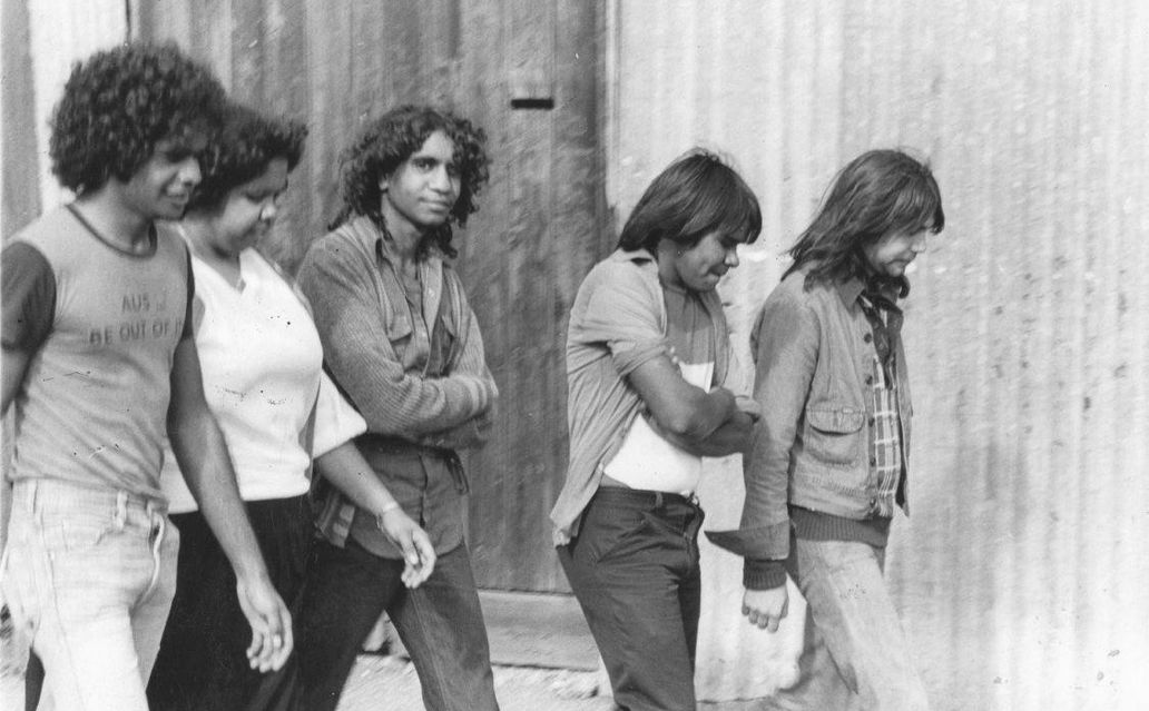 A black and white photo of the young members of No Fixed Address walking along a street
