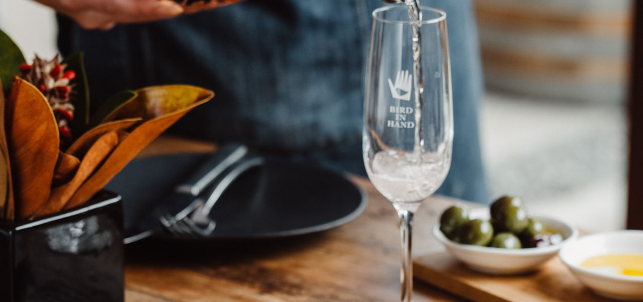 A glass of champagne being poured behind a plate of food