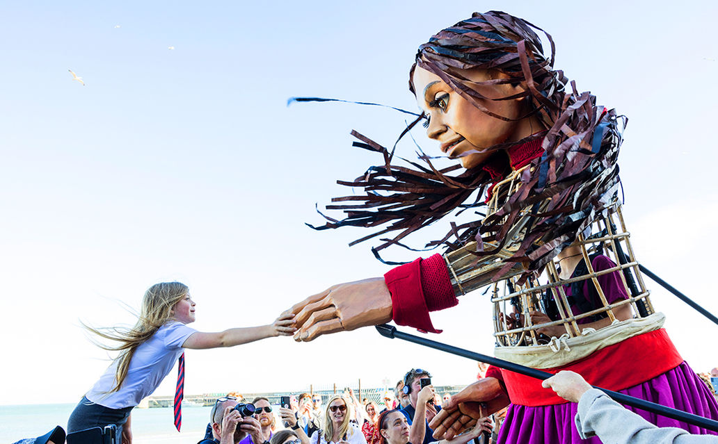 Little Amal giant puppet holding hands with a young girl