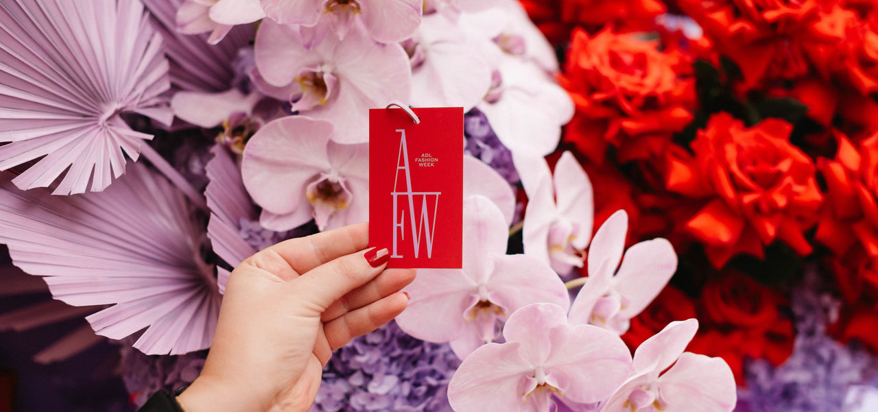 Floral arrangement in the AFW 2023 colours of lilac and red, with someone holding a tag in front that says AFW