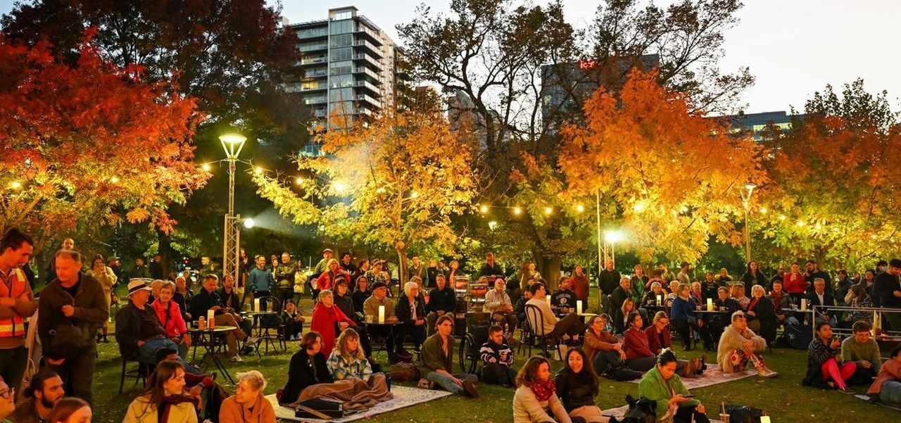 Crowds of people sitting in the park at dusk.