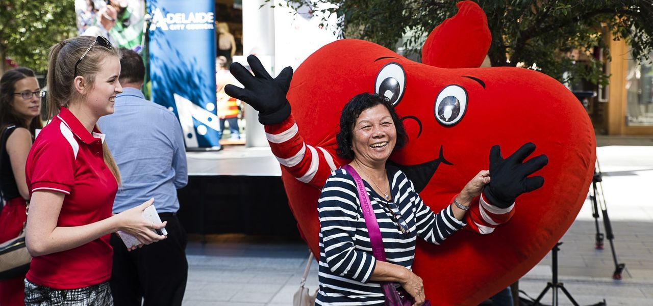 A woman smiling and waving in front of a person in a heart costume